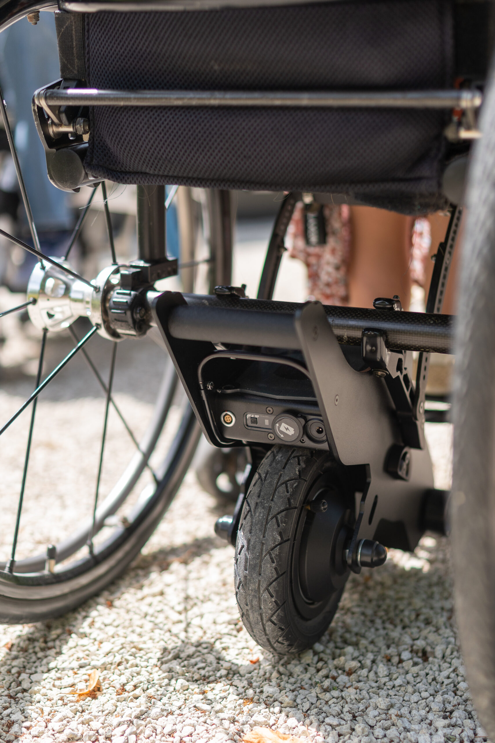 Yomper Power Assist shown mounted to the rear axle of a manual wheelchair, highlighting the in-line, low-profile design.