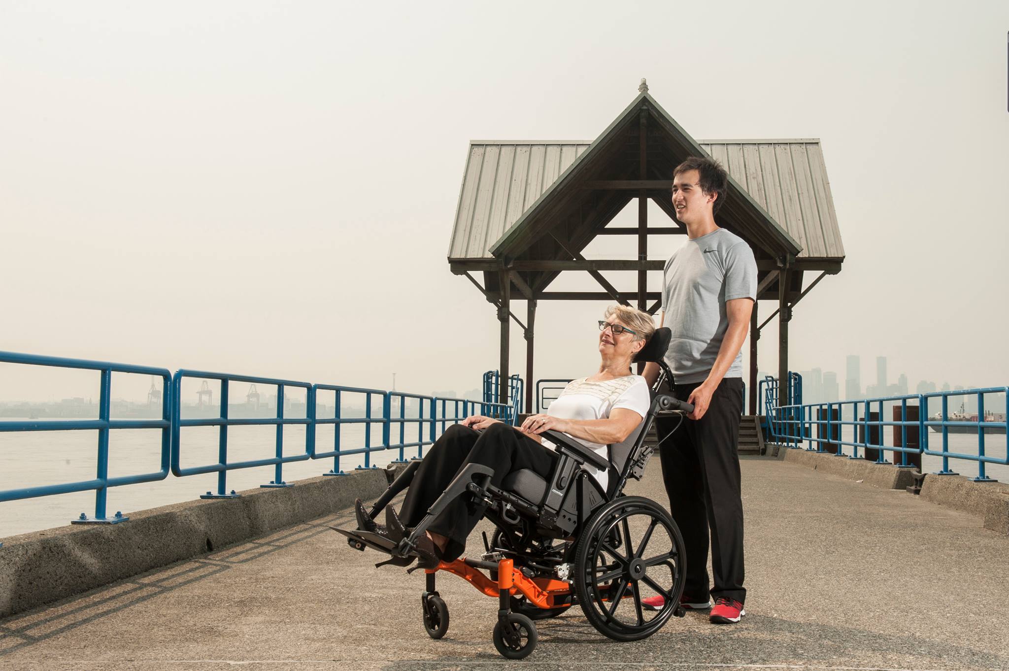 PDG fuze tilt in space wheelchair with caregiver pushing along a pier near the waterfront