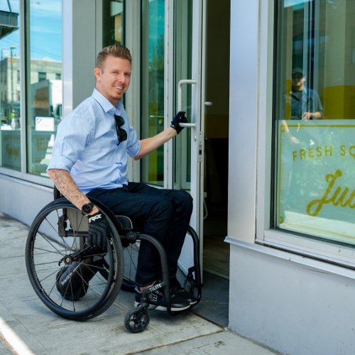 Active user in Manual wheelchair with power assist entering a café through an accessible doorway