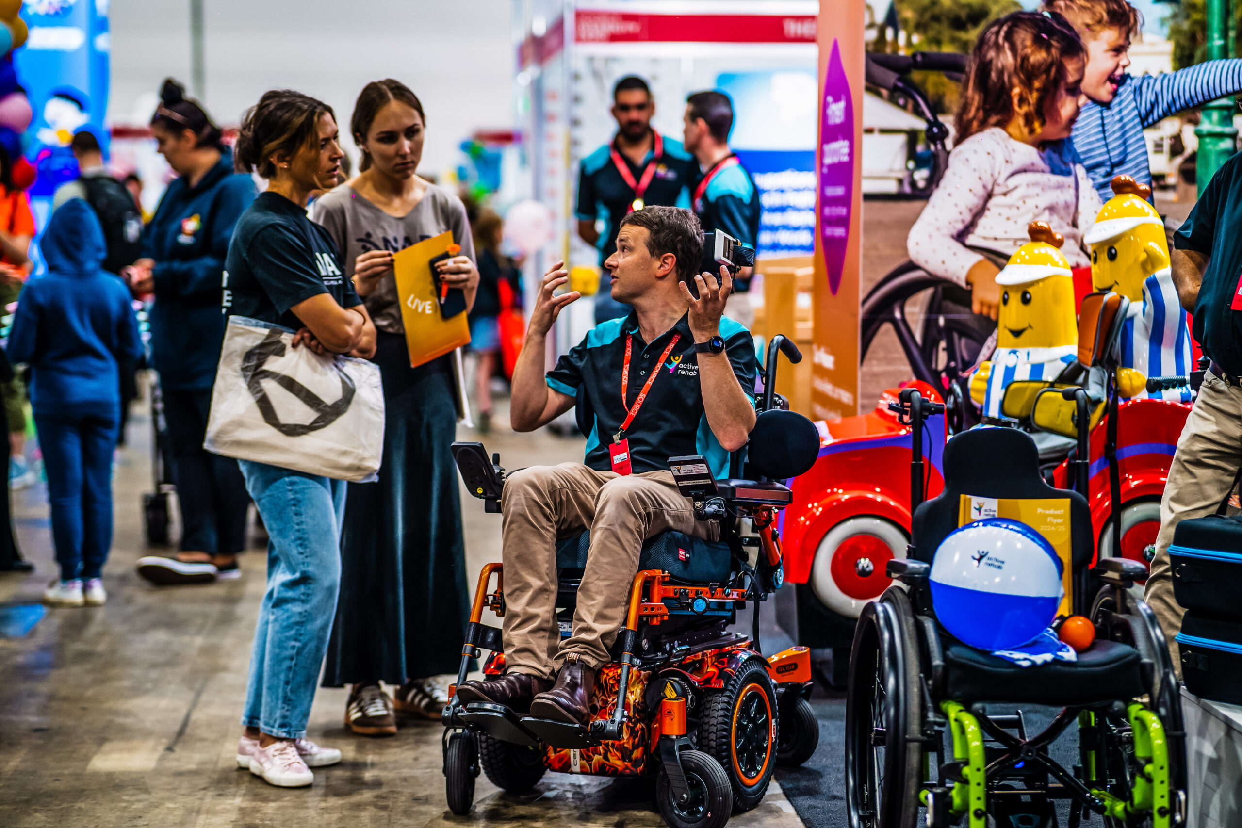 mobility expo demonstration with powered wheelchair user showcasing assistive technology to visitors